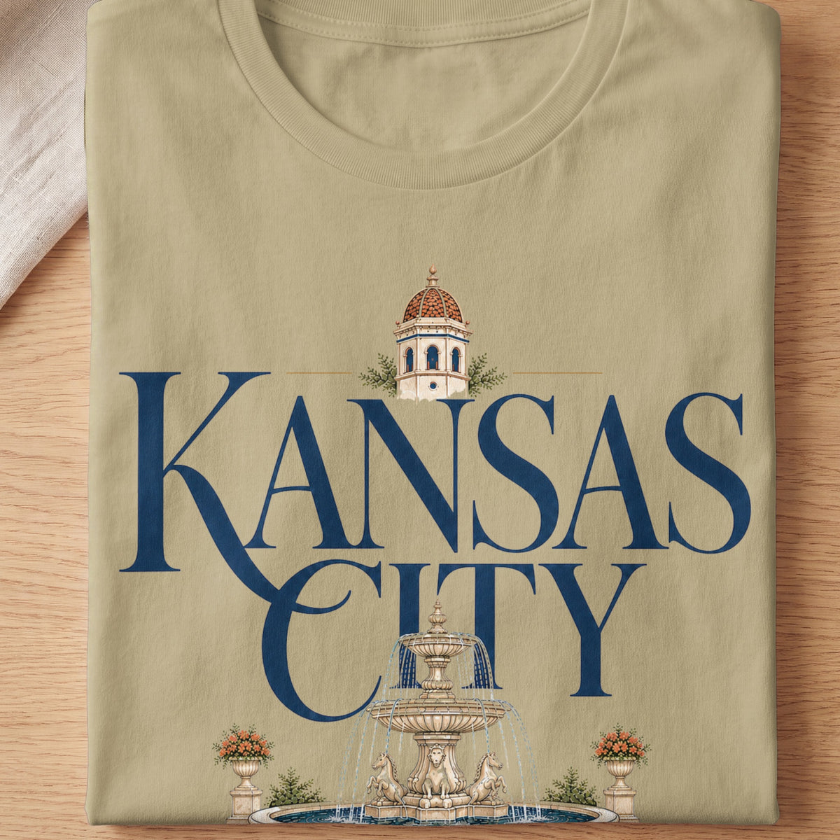 Tan t-shirt with "Kansas City" text, a building, and a fountain graphic.