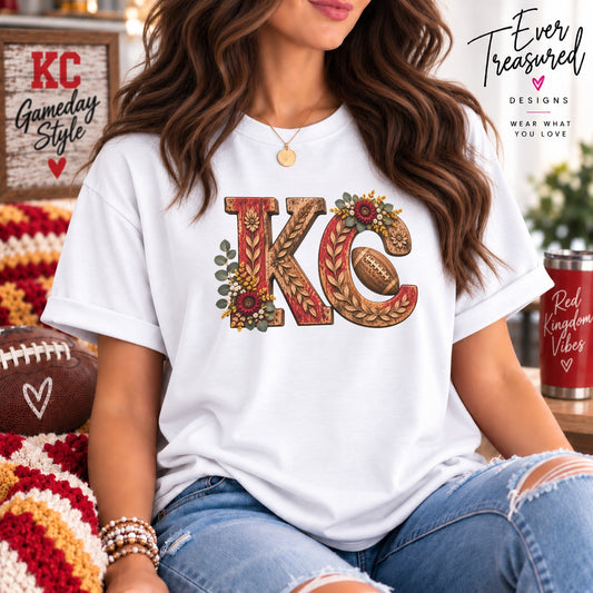 White t-shirt with "KC" graphic featuring wood texture, floral accents, and a football.