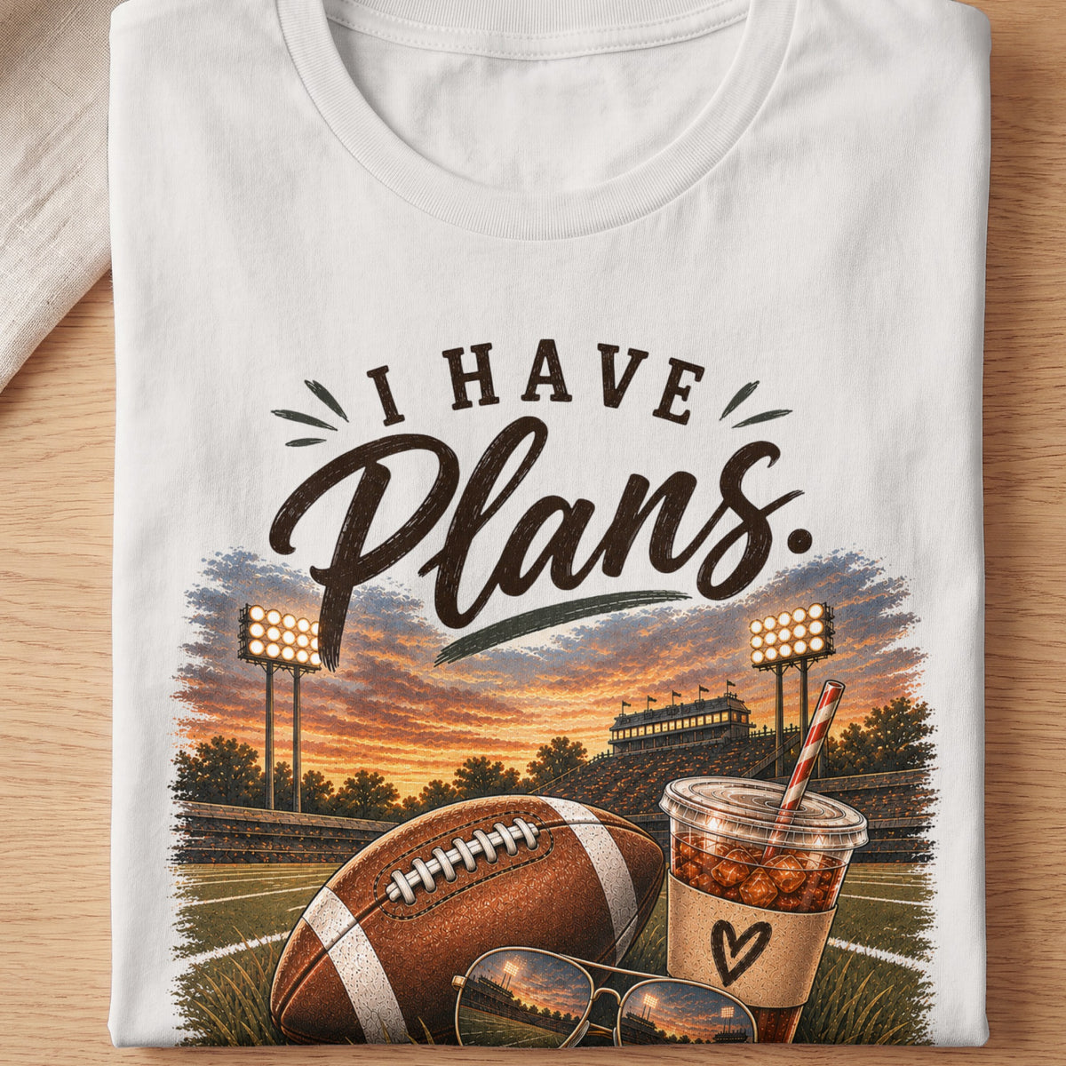 White t-shirt with "I Have Plans" text, football, stadium, and iced drink.