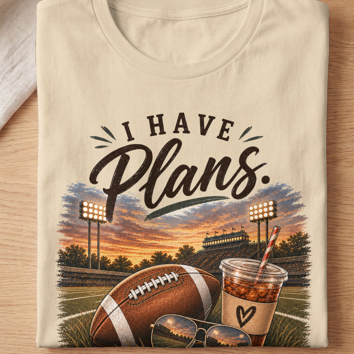 T-shirt graphic with "I HAVE Plans." text over football field, stadium, and drink.