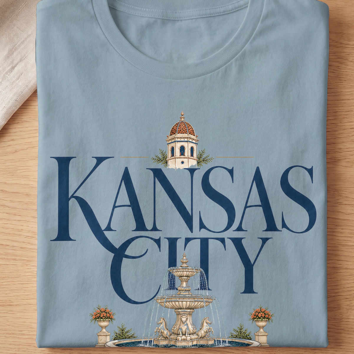 Light blue t-shirt with "Kansas City" text, fountain, and architecture.