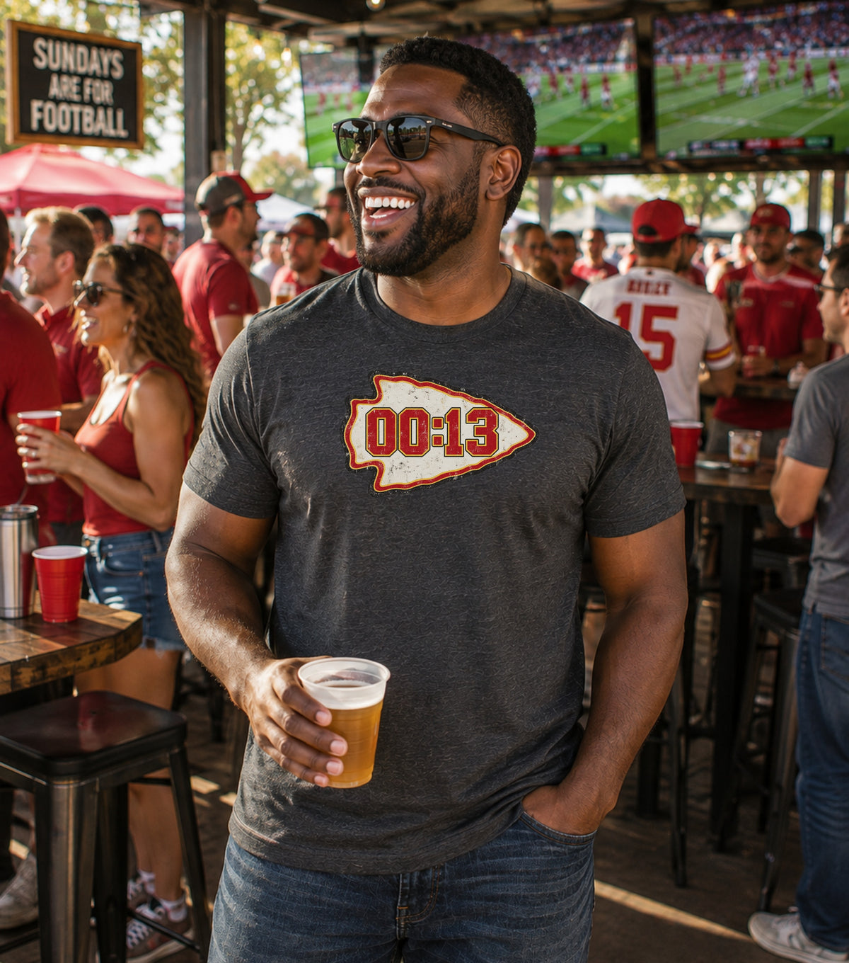 Man in dark t-shirt with "00:13" arrowhead logo holding beer cup.