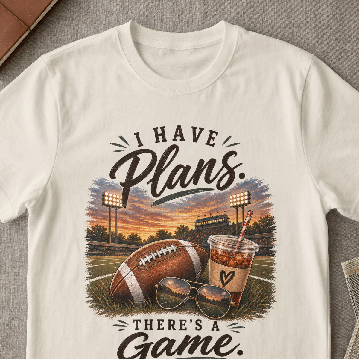 Cream t-shirt with "I Have Plans. There's A Game." text and football graphic.