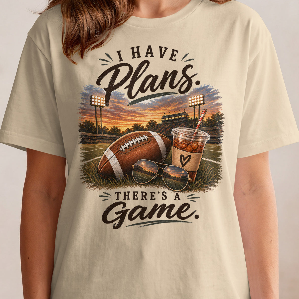 Cream t-shirt with "I Have Plans. There's A Game." text and football scene.