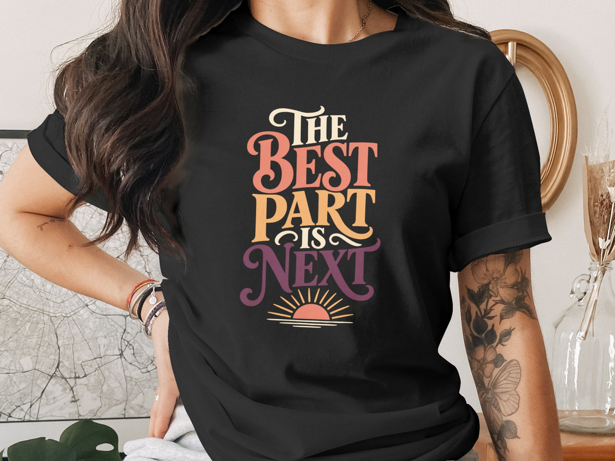 Black t-shirt with colorful text reading "THE BEST PART IS NEXT" and a sunset graphic.