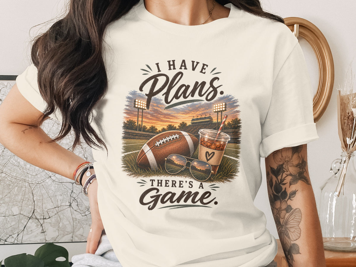 T-shirt graphic with football, drink, sunglasses, and text: "I HAVE Plans. THERE'S A Game."