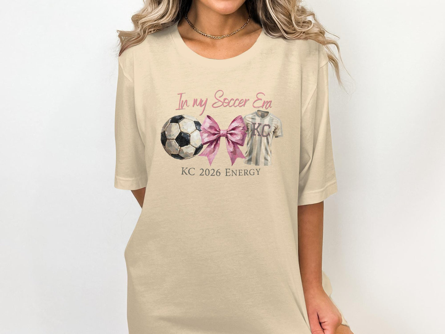Cream t-shirt with "In my Soccer Era KC 2026 Energy" and soccer ball graphic.