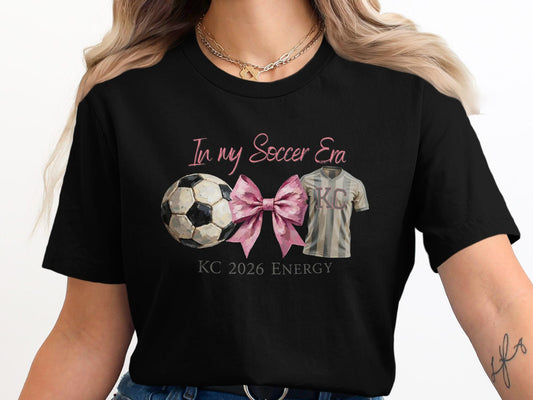 T-shirt with soccer ball, pink bow, and "KC 2026 Energy" text.
