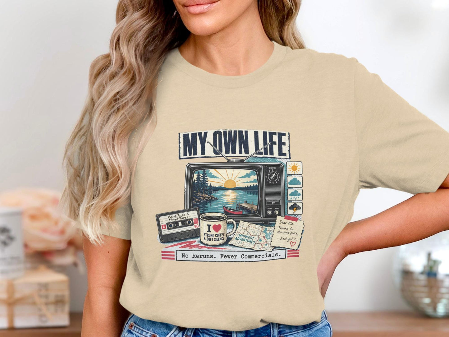 T-shirt graphic with retro TV showing lake scene, cassette tape, coffee mug, map, and text.
