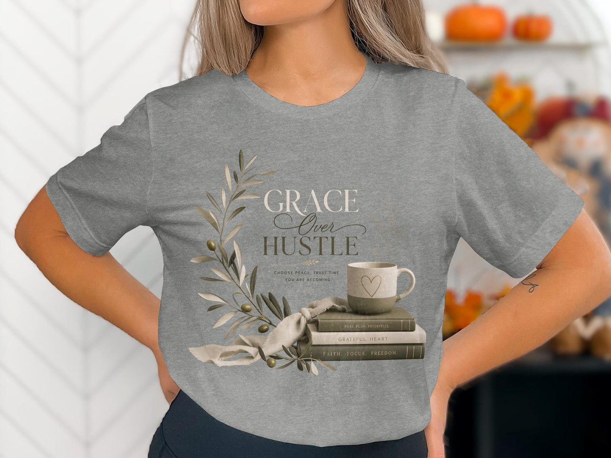 Grey t-shirt with "GRACE Over HUSTLE" text, books, and mug graphic.