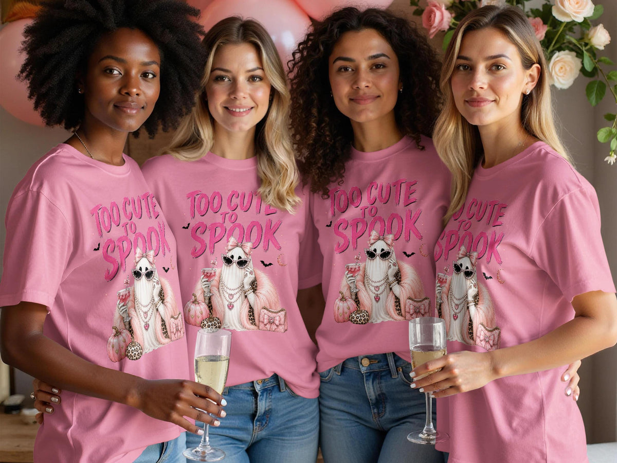 Four women in pink t-shirts featuring a "Too Cute to Spook" ghost graphic.