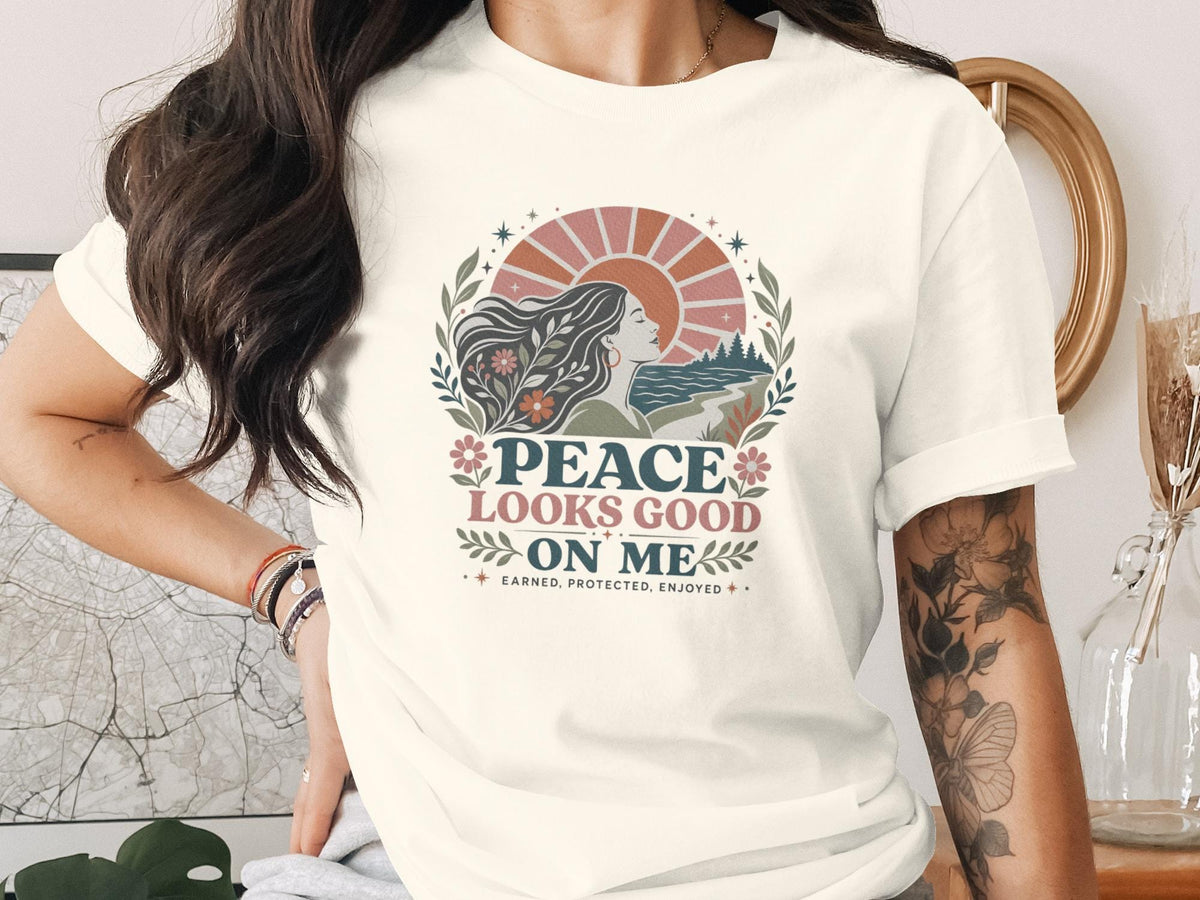Graphic tee with "Peace Looks Good On Me" text and woman with flowing hair by sunset.