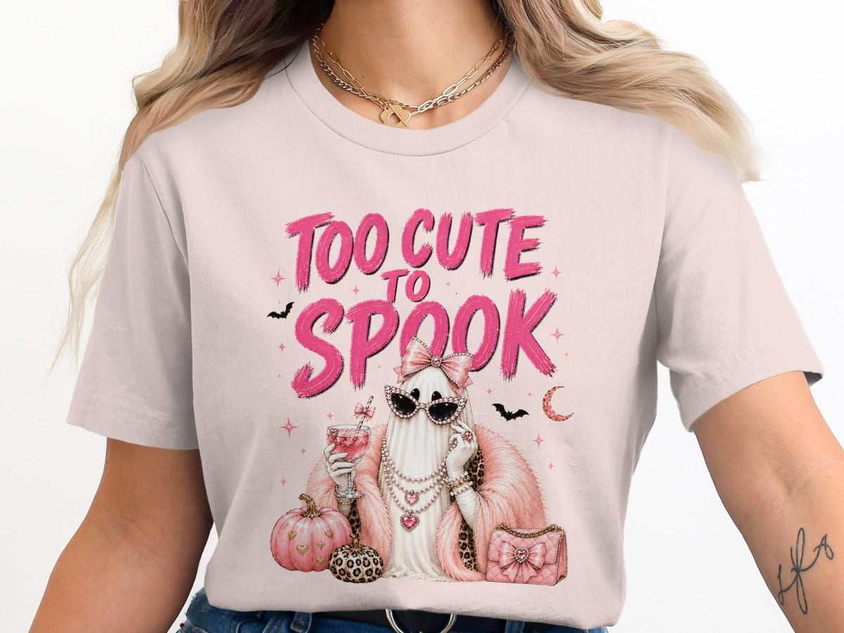 T-shirt graphic with pink text "TOO CUTE TO SPOOK" featuring a ghost with sunglasses and pearls.