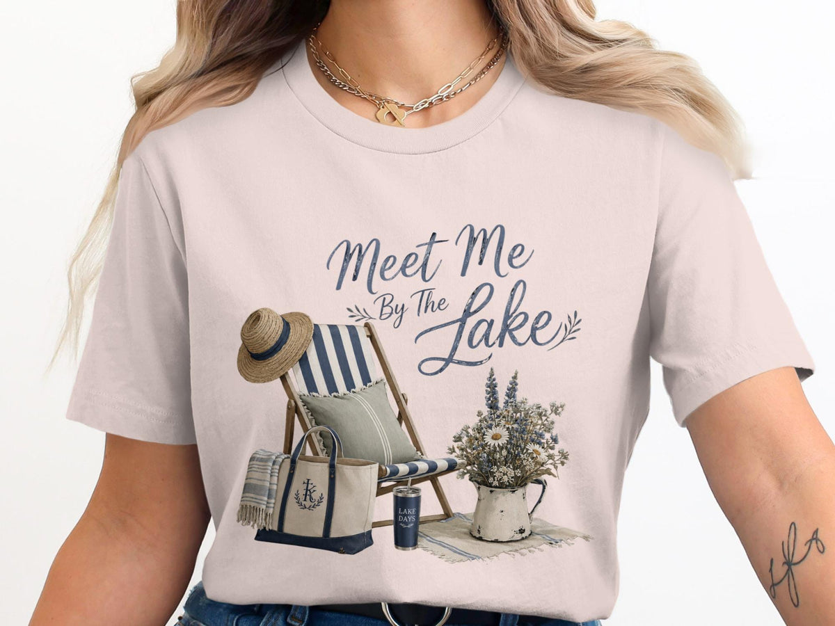 T-shirt graphic with "Meet Me By The Lake" text, beach chair, tote bag, and flowers.